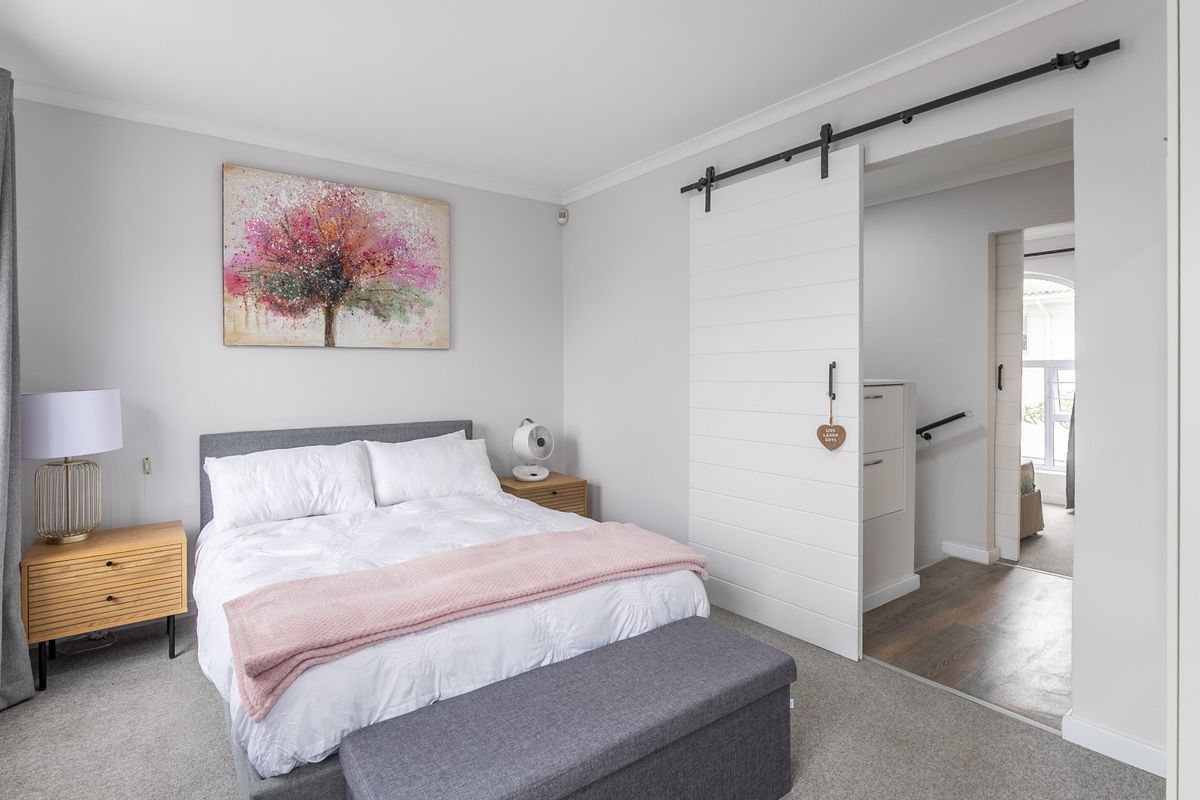 A well-maintained bedroom featuring neutral wall tones, carpeted flooring, and a modern white sliding barn door leading to an adjacent hallway.