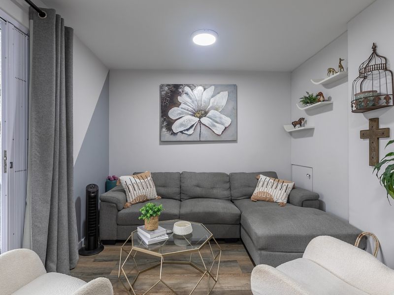 A cozy living room featuring laminate flooring, recessed lighting, and a large sliding glass door providing access to an outdoor patio area.