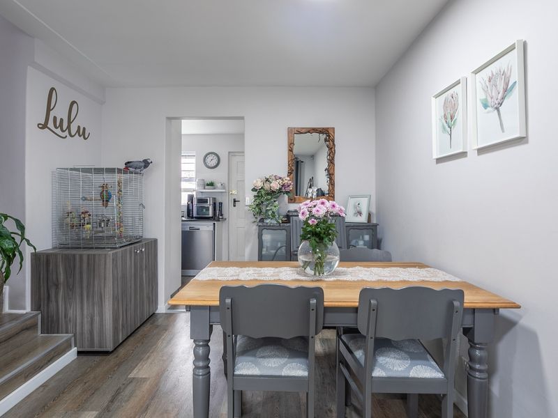 A well-maintained dining area featuring modern laminate flooring and an open-plan layout leading to the kitchen.