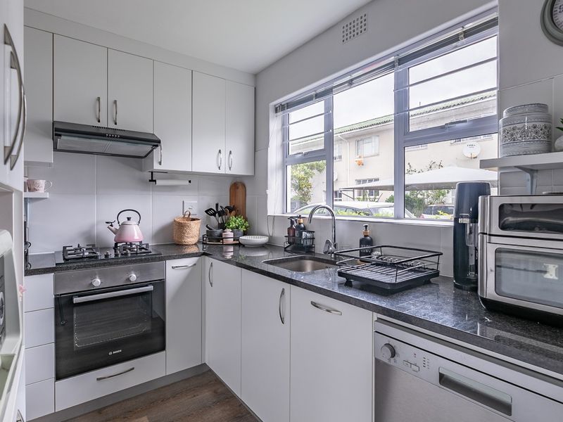 A well-maintained kitchen featuring white cabinetry, granite countertops, a built-in oven with gas hob, and a tiled backsplash with ample natural light.