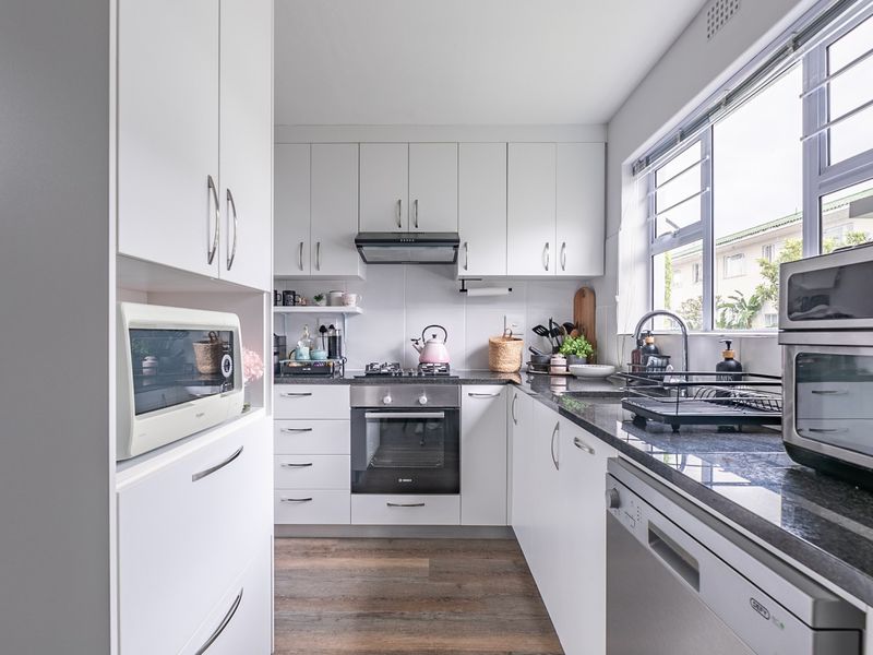 A modern, well-maintained kitchen featuring white cabinetry, granite countertops, a gas hob, and an integrated oven, offering a clean and functional workspace.