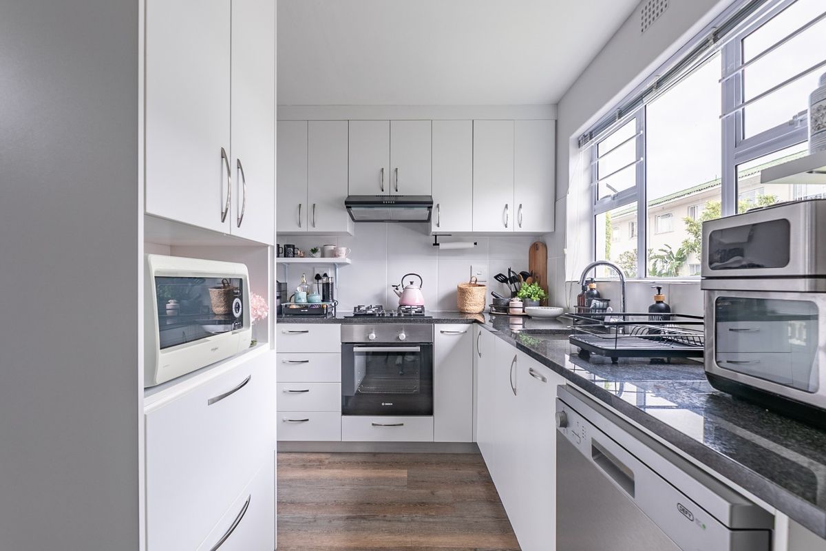 A modern, well-maintained kitchen featuring white cabinetry, granite countertops, a gas hob, and an integrated oven, offering a clean and functional workspace.
