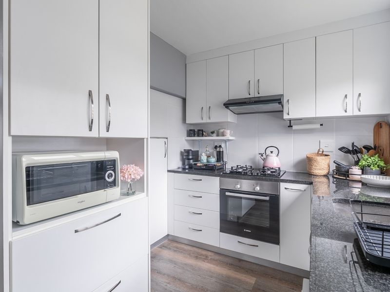 Modern kitchen featuring white cabinetry, granite countertops, a gas hob, built-in oven, and a tiled backsplash with ample storage space.