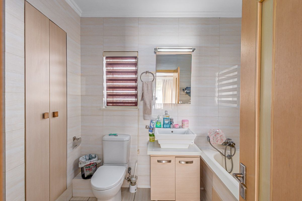 A functional bathroom featuring a built-in vanity with basin, a bathtub with shower mixer, a toilet, and ample built-in storage cabinetry.