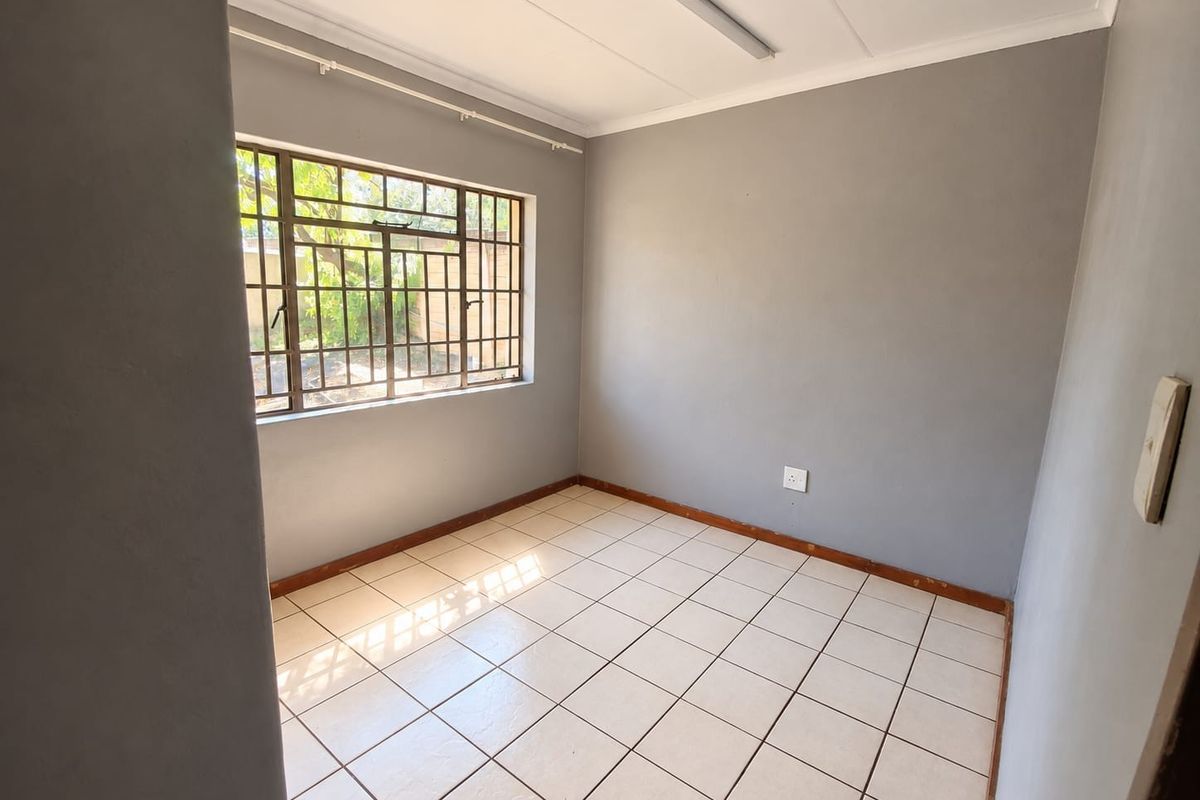 A vacant bedroom featuring neutral grey walls, tiled flooring, and a window fitted with security bars.
