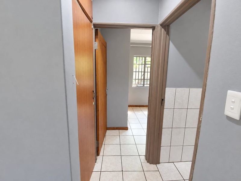 A functional hallway featuring tiled flooring, built-in wooden cupboards, and access to an adjacent room with a window.