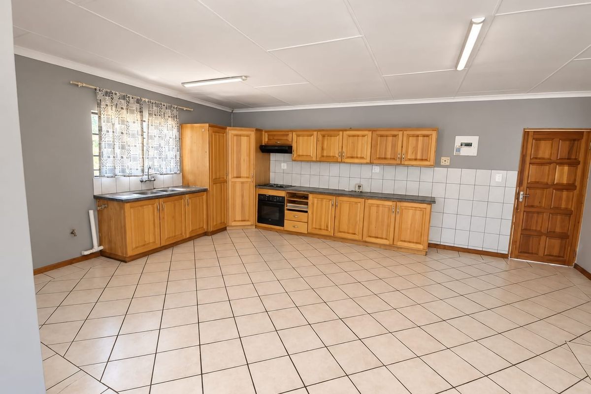 Spacious kitchen featuring wooden cabinetry, built-in oven, hob, extractor fan, and tiled flooring. The area is clean and ready for modern updates.