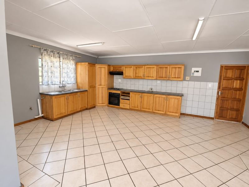 Spacious kitchen featuring wooden cabinetry, built-in oven, hob, extractor fan, and tiled flooring. The area is clean and ready for modern updates.