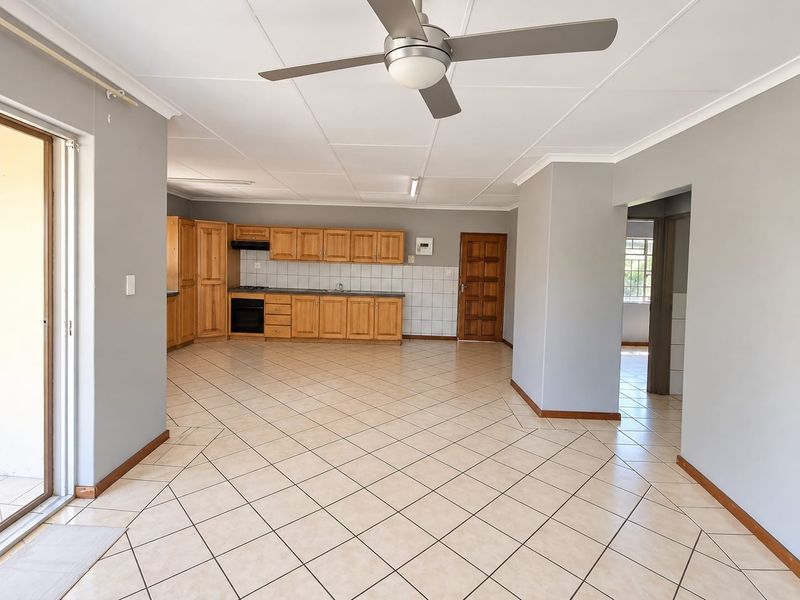 Spacious open-plan living and kitchen area featuring tiled floors, a ceiling fan, and traditional wooden cabinetry with integrated appliances.
