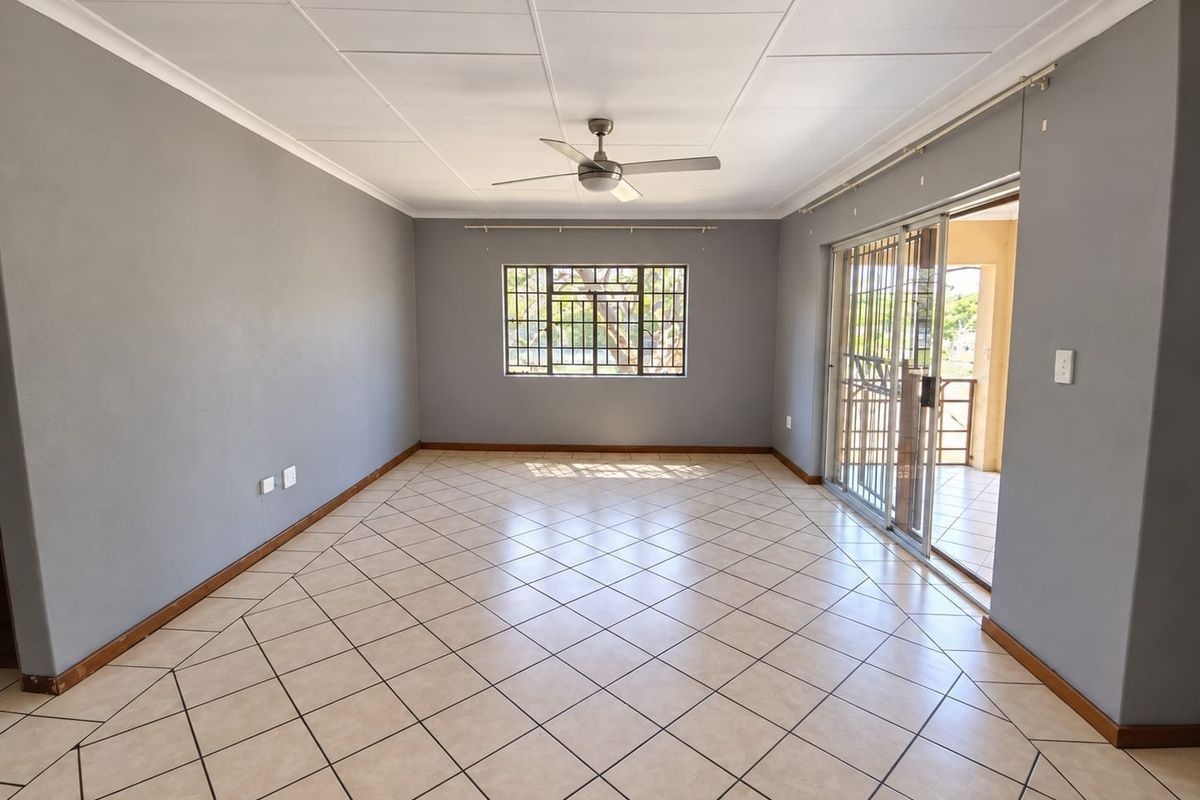 Spacious, empty living area featuring neutral grey walls, tiled flooring, a ceiling fan, and sliding glass doors leading to an outdoor patio.
