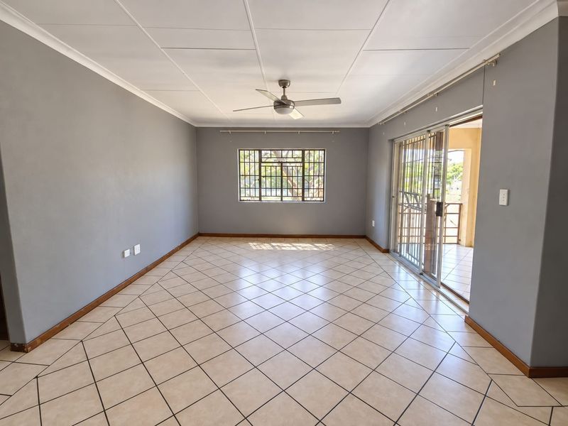 Spacious, empty living area featuring neutral grey walls, tiled flooring, a ceiling fan, and sliding glass doors leading to an outdoor patio.