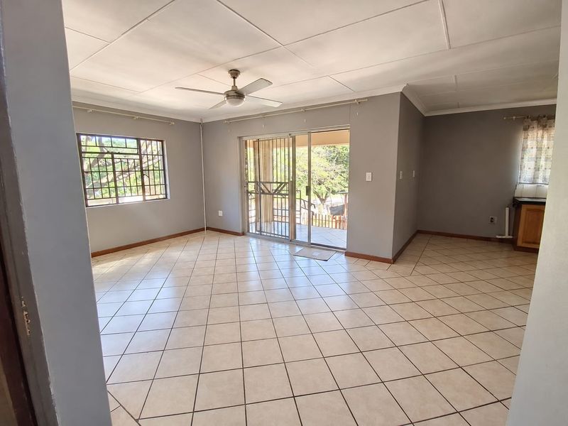 Spacious open-plan living area featuring neutral grey walls, tiled flooring, a ceiling fan, and sliding glass doors leading to an outdoor patio.