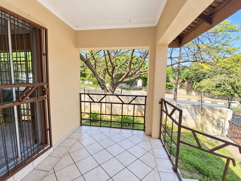 A covered patio area featuring tiled flooring and metal security balustrades, overlooking the front garden and street.