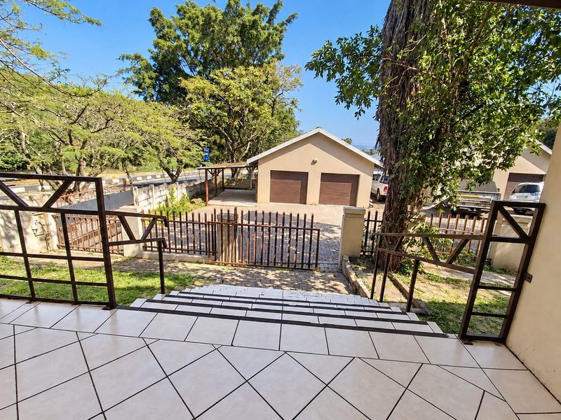 View from the entrance steps overlooking a paved driveway, double garage, and secure perimeter fencing with mature trees.