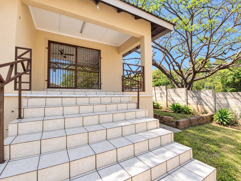 A covered patio area featuring a wide tiled staircase with metal handrails and a secure metal gate entrance, overlooking a garden space.
