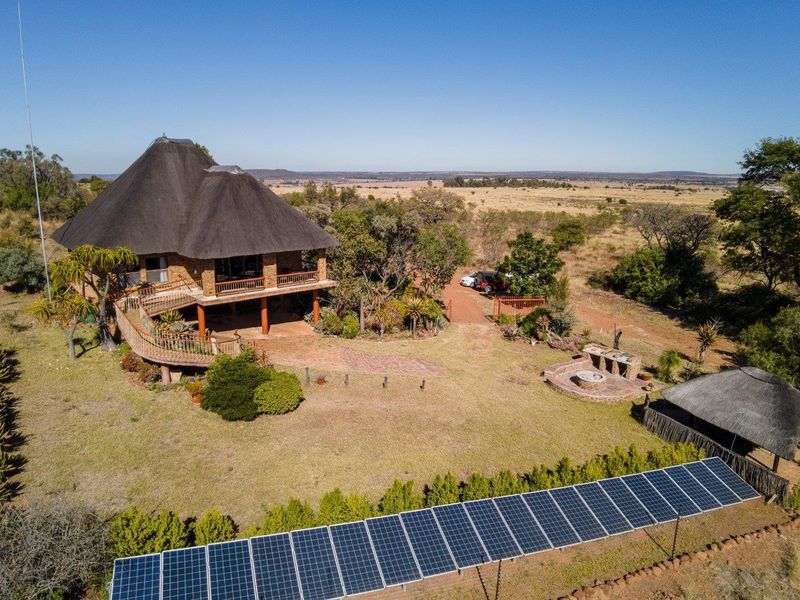 Aerial view of a farm property featuring a thatched-roof house, raised deck, solar panel array, and a dedicated outdoor braai and boma area.
