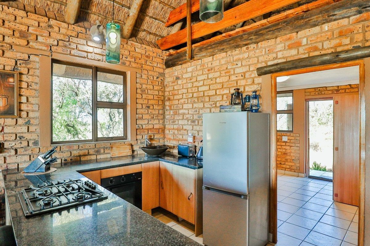 Rustic kitchen featuring exposed brick walls, a high thatched ceiling with timber beams, granite countertops, and a built-in gas hob and oven.