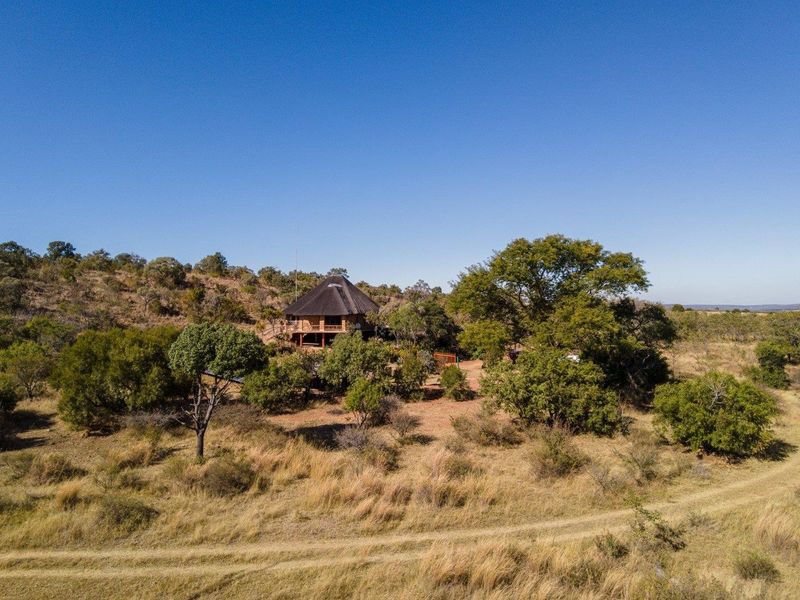 Aerial view of a rural farm property featuring a dwelling with a traditional thatched roof set within a natural landscape.