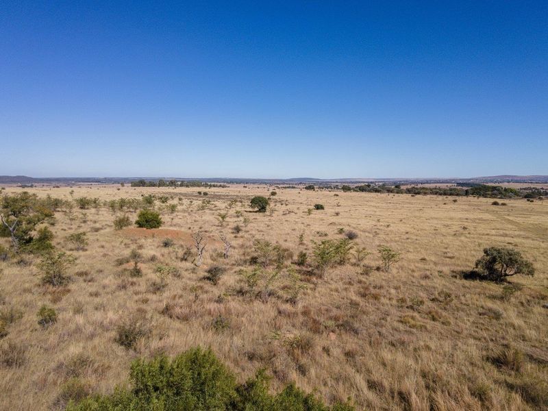 An expansive aerial view of the open farm landscape, showcasing the natural terrain and vegetation under a clear blue sky.