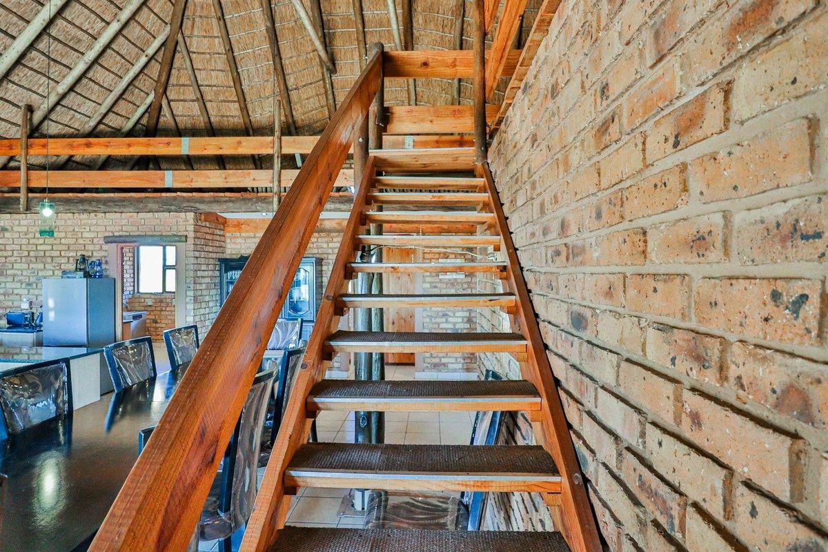 Open plan living area featuring rustic exposed brick walls, a traditional thatched roof with exposed timber beams, and a central timber staircase.