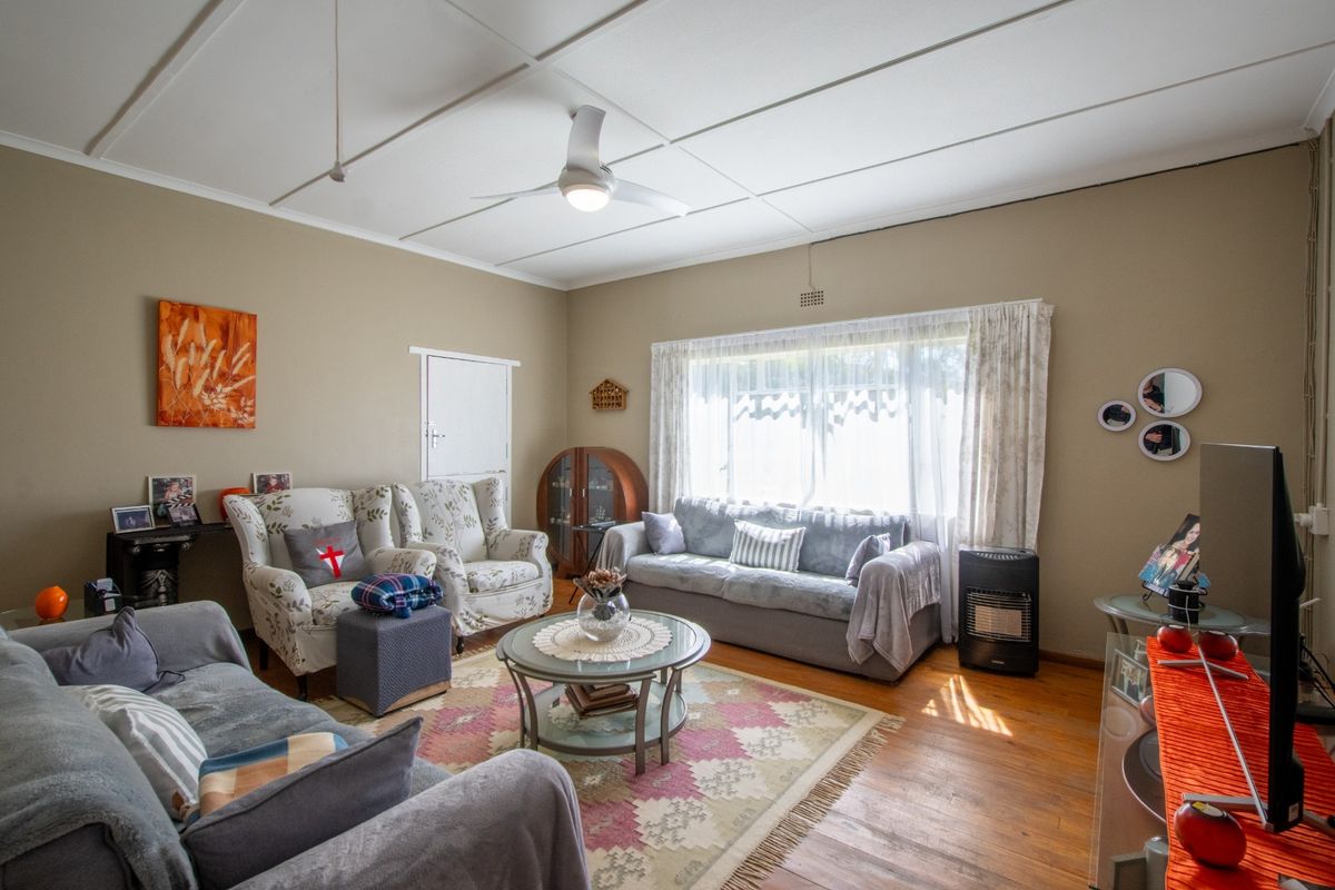 A comfortable living room featuring warm hardwood flooring, a ceiling fan, and large windows that provide ample natural light.