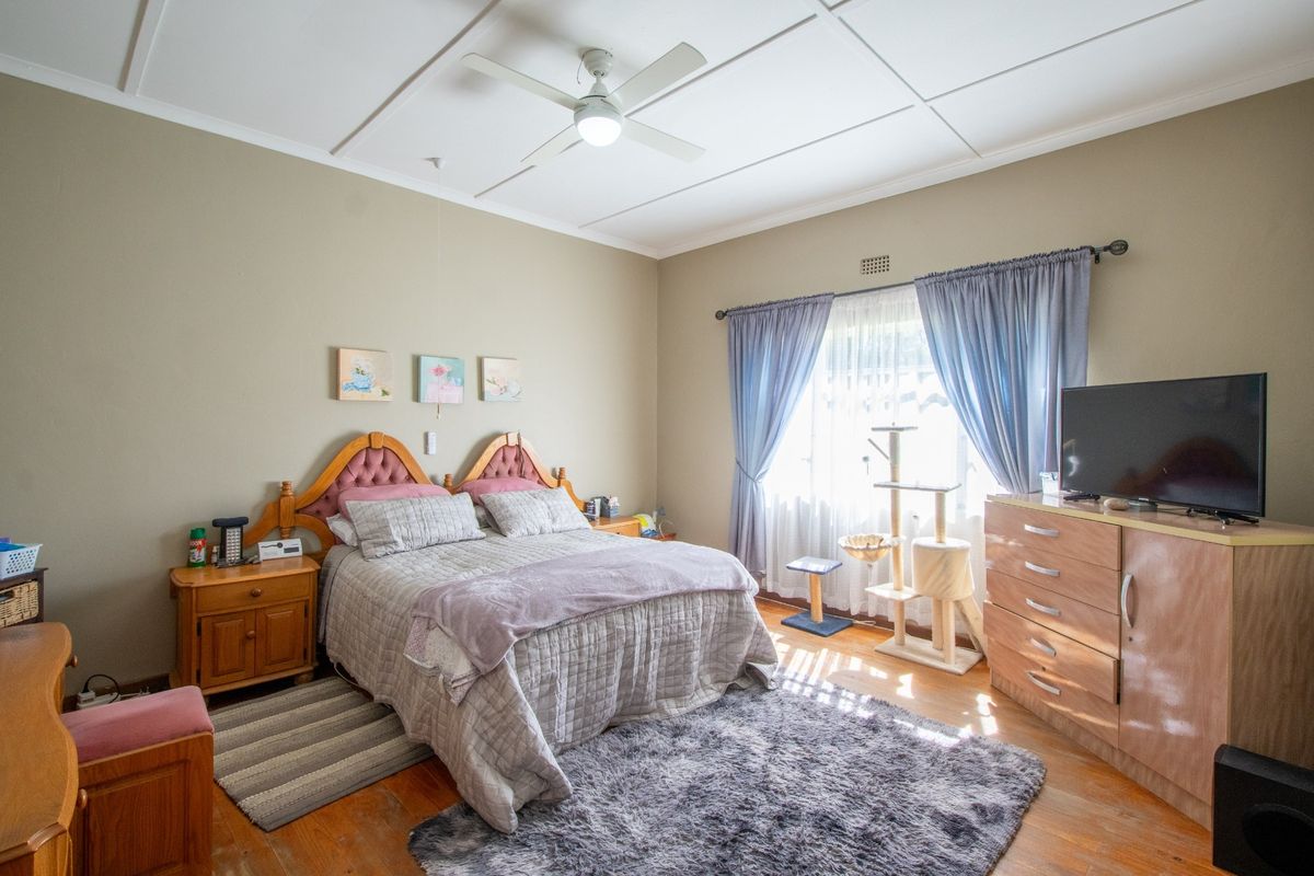 A well-lit bedroom featuring timber flooring, a ceiling fan, and a ventilation grille, offering a comfortable and functional living space.