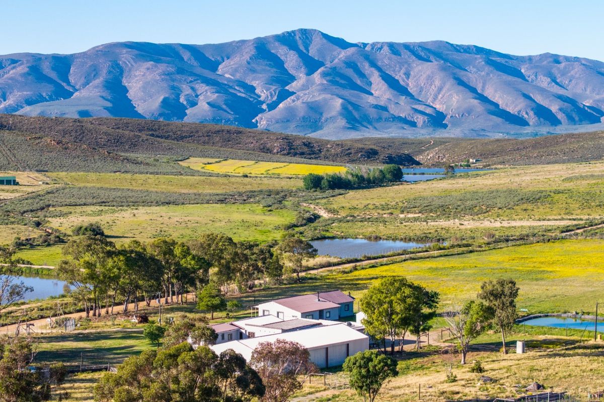 An aerial view of the farm property featuring multiple buildings, dams, and expansive surrounding landscape with mountain views.