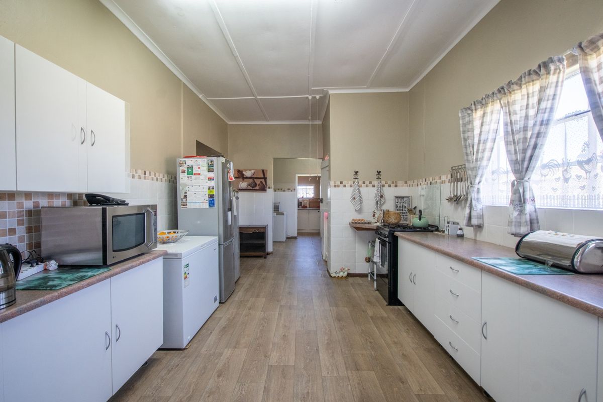 A functional kitchen featuring white cabinetry, laminate countertops, a tiled backsplash, and wood-look laminate flooring, offering a practical layout for daily meal preparation.