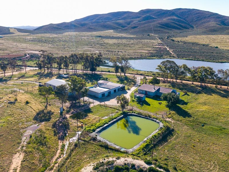 Aerial view of the farm property featuring a main dwelling, multiple outbuildings, a large dam, and expansive surrounding landscape.
