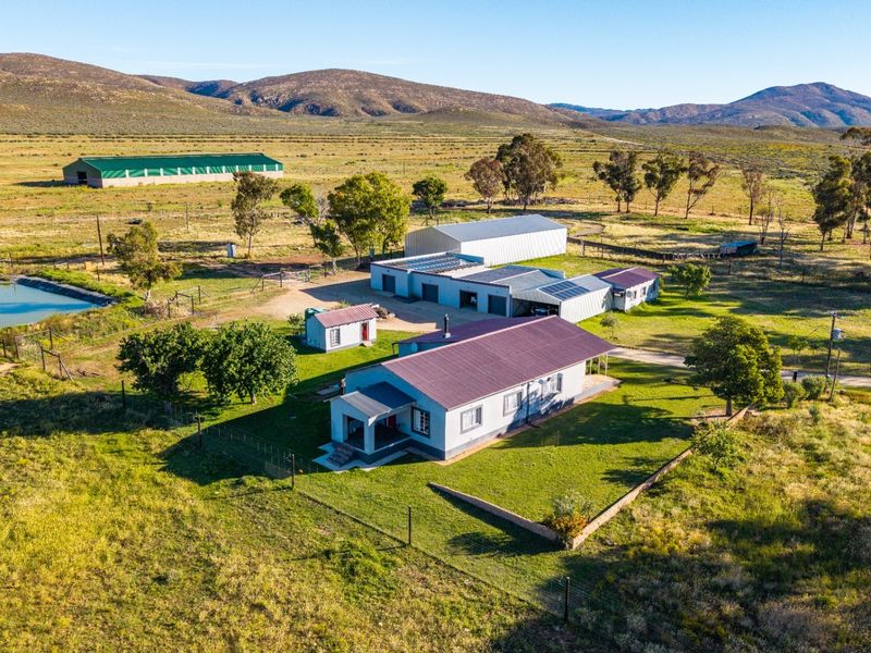 Aerial view of a rural farm property featuring a main residence, multiple outbuildings, solar installations, and a private dam set within a vast landscape.