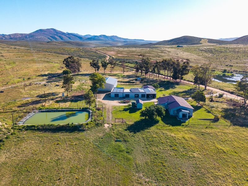 Aerial view of a rural farm property featuring a main dwelling, multiple outbuildings, a farm dam, and expansive surrounding landscape.