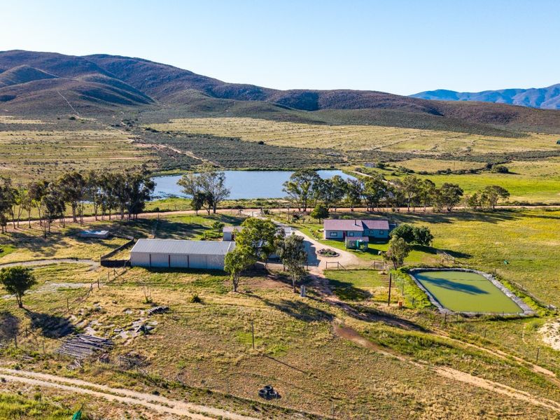 Aerial view of a rural farm property featuring a main dwelling, large metal shed, and private dam set against a scenic mountain landscape.