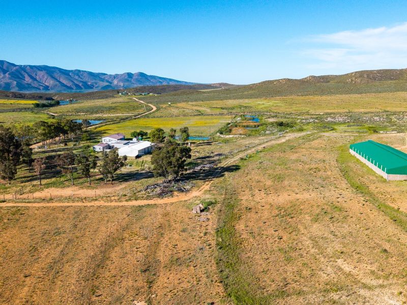 Aerial view of a large farm property featuring multiple buildings, a dam, and extensive open grazing land set against a mountain backdrop.