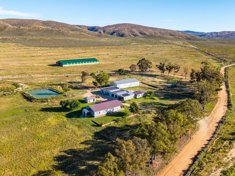 Aerial view of a rural farm property featuring multiple outbuildings, solar installations, a private dam, and extensive surrounding grazing land.