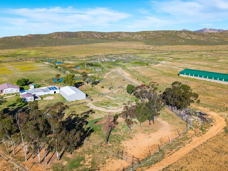 Aerial view of a rural farm property featuring a main residence, multiple outbuildings, a large agricultural shed, and expansive surrounding grazing land.