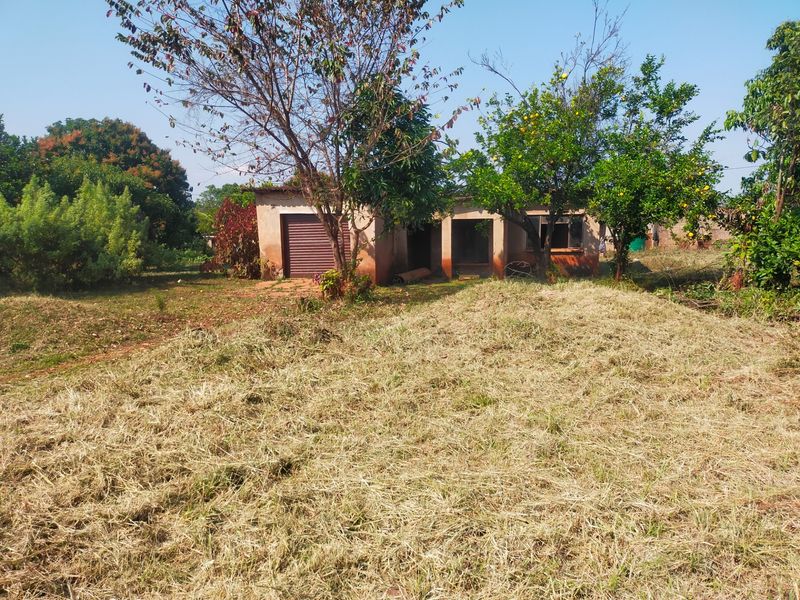 Front view of a residential property featuring a roller garage door and mature garden area on a large plot.