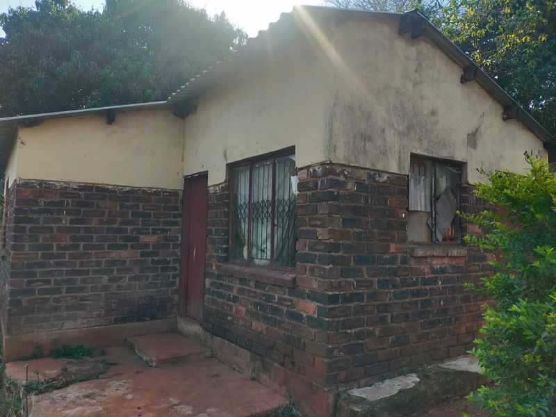 Rear exterior view of a small brick structure showing significant wear to the facade, roof, and window frames.