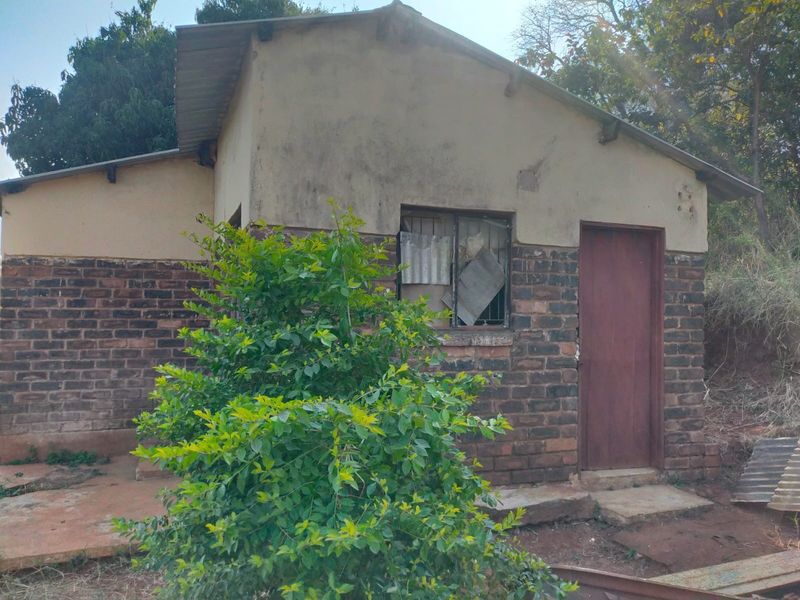 Rear exterior view of a small brick house showing signs of significant weathering and maintenance requirements on the facade and window fixtures.
