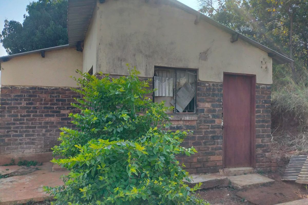 Rear exterior view of a small brick house showing signs of significant weathering and maintenance requirements on the facade and window fixtures.