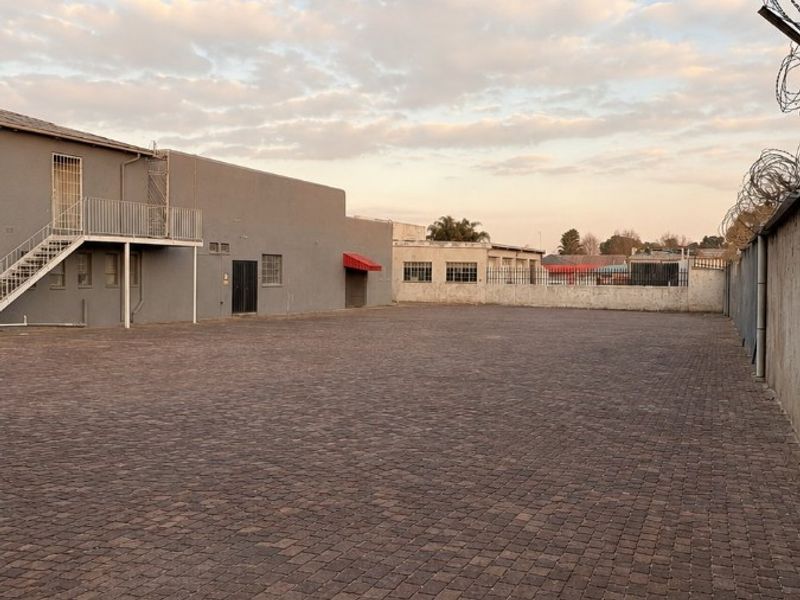 A spacious, paved commercial rear yard featuring an external staircase, secure perimeter walling, and razor wire fencing.