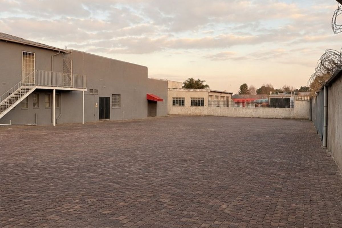A spacious, paved commercial rear yard featuring an external staircase, secure perimeter walling, and razor wire fencing.