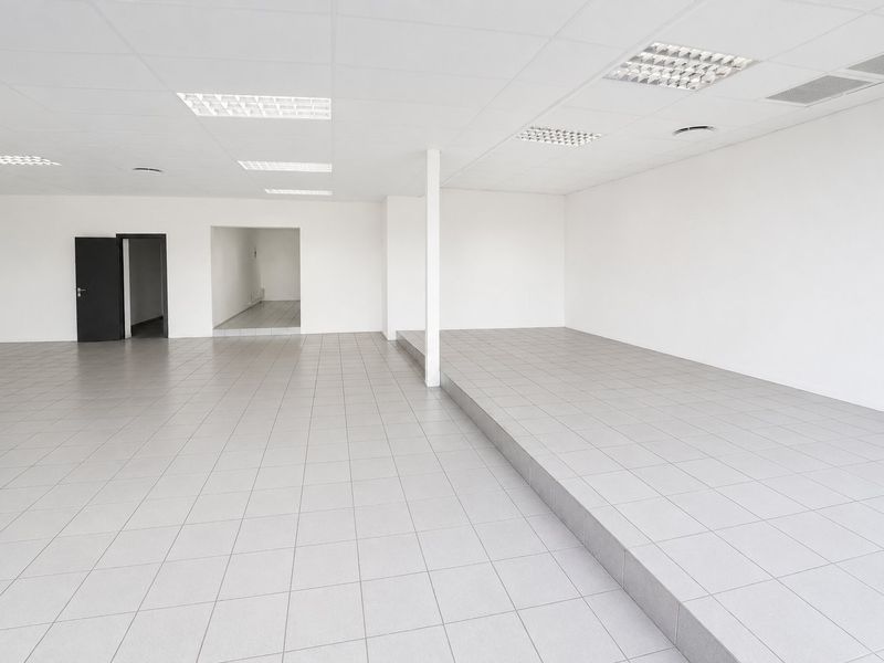 Spacious open-plan commercial unit featuring a raised platform, neutral ceramic tiling, and a suspended ceiling with integrated lighting, suitable for various business applications.