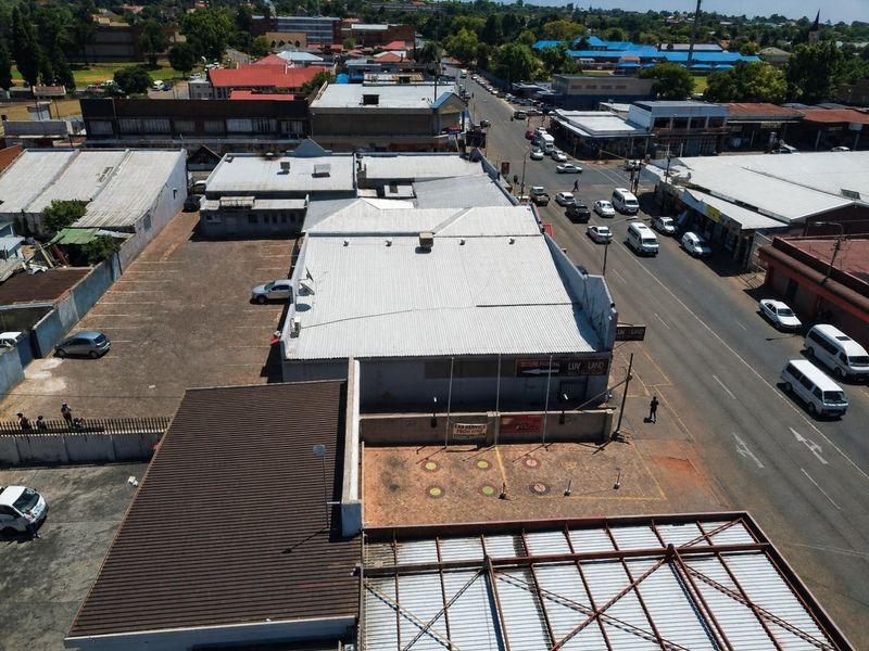Aerial view of a commercial property featuring a large corrugated metal roof, paved parking area, and street-level access in a busy urban setting.