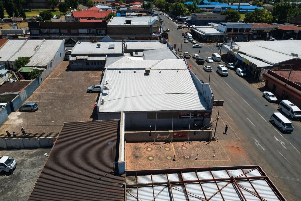 Aerial view of a commercial property featuring a large corrugated metal roof, paved parking area, and street-level access in a busy urban setting.
