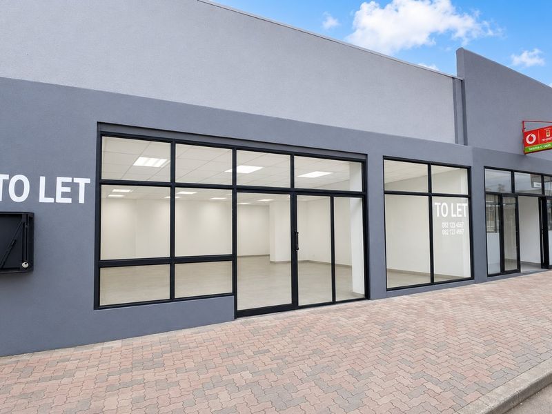 Modern commercial storefront with large glass windows, black aluminium frames, and paved sidewalk access, suitable for retail or office use.
