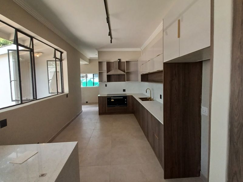 Modern, spacious kitchen featuring sleek two-tone cabinetry, stone countertops, integrated oven, extractor fan, and high-quality brass fixtures with ample natural light.