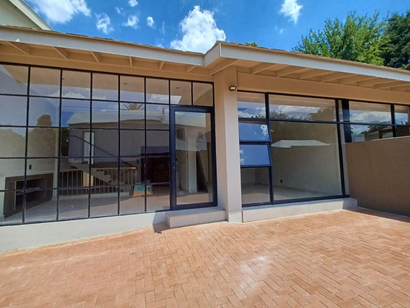 Rear exterior view featuring a brick paved patio and large steel-framed glass windows and doors, providing a seamless transition to the interior living space.