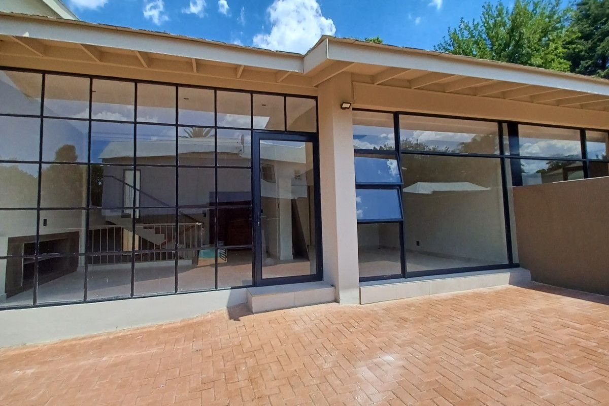Rear exterior view featuring a brick paved patio and large steel-framed glass windows and doors, providing a seamless transition to the interior living space.