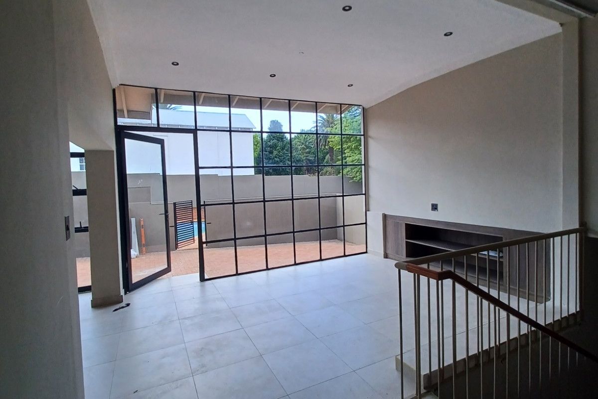 Spacious living area featuring large steel-framed windows, tiled flooring, recessed lighting, and a built-in media unit, overlooking the outdoor patio area.
