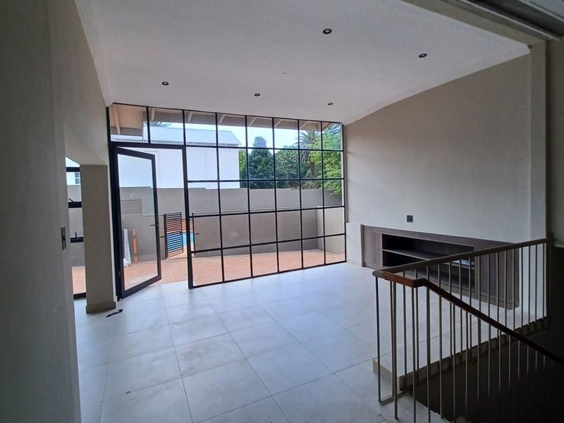 Spacious living area featuring large steel-framed windows, tiled flooring, recessed lighting, and a built-in media unit, overlooking the outdoor patio area.